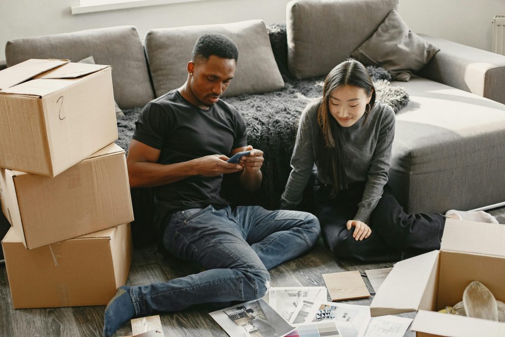 Young interracial couple sitting on floor while unpacking boxes and checking a mobile phone at home.